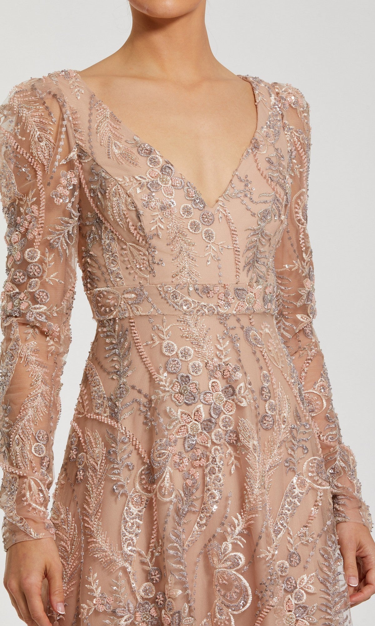 A person wearing the Mac Duggal 68908 long formal dress—featuring blush pink fabric, silver floral embroidery, long sleeves, and a deep V-neckline—an elegant choice for a mother-of-the-bride gown.